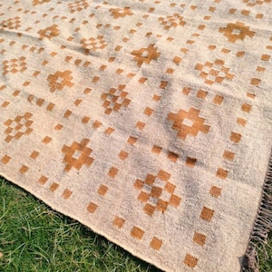 May include: Beige and brown patterned rug with a geometric design. The rug features repeating square and cross-like patterns in a warm brown colour against a beige background. The rug has a fringed edge.