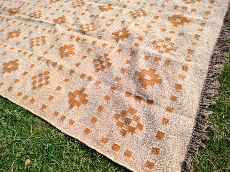 May include: Beige and brown patterned rug with a geometric design. The rug features repeating square and cross-like patterns in a warm brown colour against a beige background. The rug has a fringed edge.
