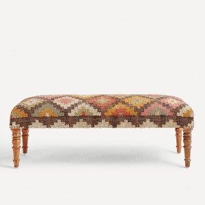 以下が含まれることがあります： カラフルな模様のクッションが付いた茶色の木製ベンチ。クッションは赤、オレンジ、黄色、緑、茶色の幾何学模様です。