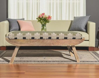 Könnte beinhalten: Ein helles Sofa mit grauen und rosa Kissen und einer gemusterten Bank. Die Bank hat ein Holzgestell und eine gewebte Oberseite mit geometrischem Design. Eine Vase mit rosa Blumen steht auf dem Sofa.
