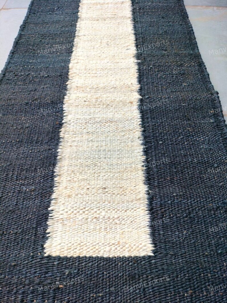 Pode incluir: Um tapete tecido preto e branco com uma faixa branca longa e estreita no centro. O tapete &eacute; feito de fibras naturais e tem uma textura &aacute;spera.