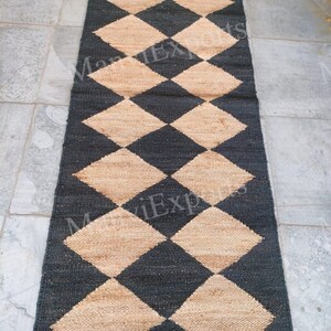 May include: A black and beige woven rug with a diamond pattern. The rug is made of natural fibers and has a rustic look.