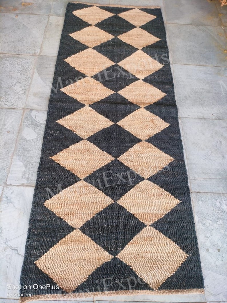 May include: A black and beige woven rug with a diamond pattern. The rug is made of natural fibers and has a rustic look.