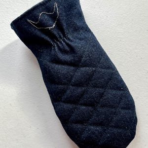 May include: A dark blue denim oven mitt with a quilted pattern. The mitt has a white embroidered design near the opening. The mitt is designed to protect hands from heat when handling hot cookware.