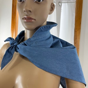 May include: A blue denim bandana tied around a mannequin's neck. The bandana is tied in a knot at the front and the ends are hanging down.