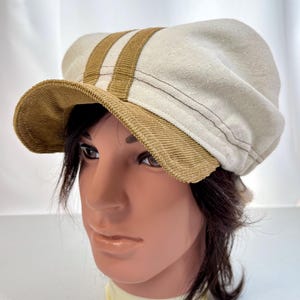 May include: A white canvas newsboy cap with brown corduroy trim and two brown stripes. The cap has a slightly curved brim.