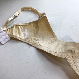 May include: A beige bra with a white label that reads "The Wilder Collection, UK Handmade". The bra has a hook and eye closure and is made of a soft, natural fabric.