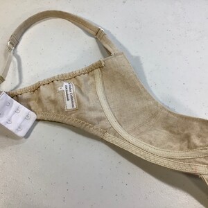 May include: Beige bra with adjustable straps and a hook and eye closure. The bra has a label that reads "Fashion Collection DK Handmade".