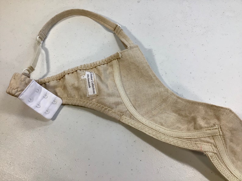 May include: Beige bra with adjustable straps and a hook and eye closure. The bra has a label that reads "Fashion Collection DK Handmade".