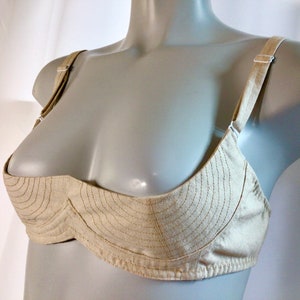 May include: A beige bra with a unique design featuring a curved, padded cup and adjustable straps.