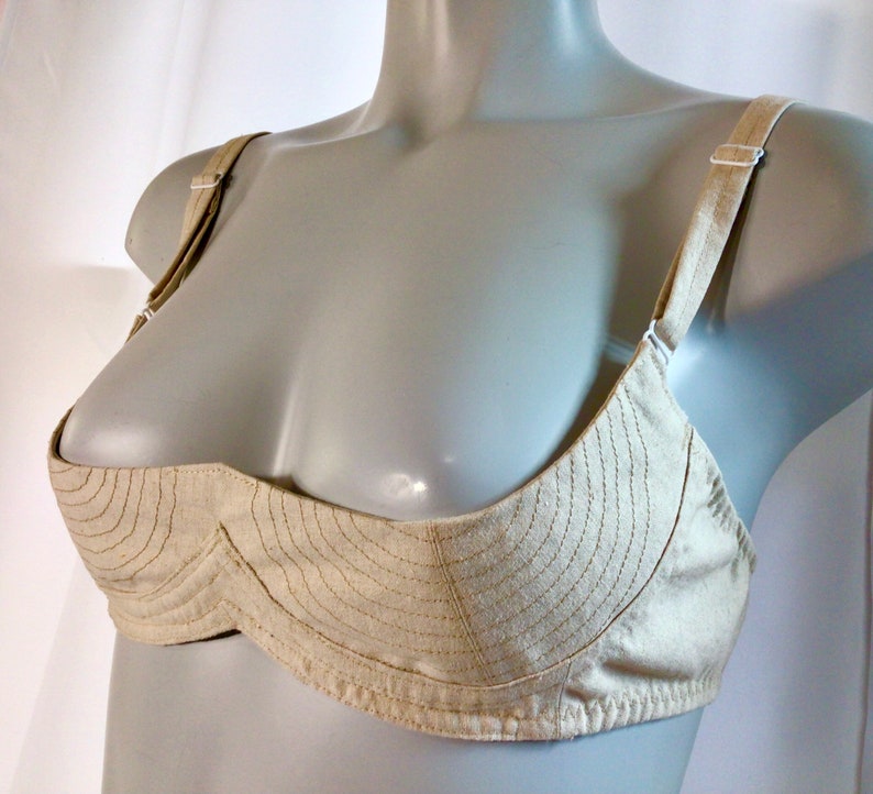 May include: A beige bra with a unique design featuring a curved, padded cup and adjustable straps.