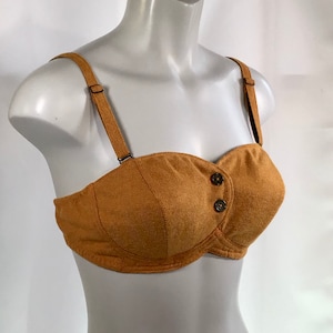 May include: A brown strapless bra with a button closure. The bra is made of a soft, textured fabric.