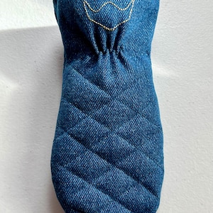 May include: A quilted denim oven mitt in a deep indigo blue. The mitt features a gold embroidered crown design near the opening. The mitt has a diamond pattern and is designed to protect hands from heat.