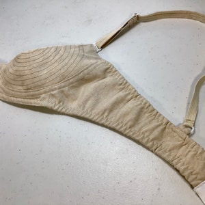 May include: A beige bra with adjustable straps and a white hook and eye closure. The bra has a padded cup with a quilted design.