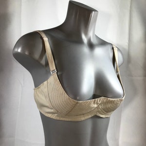 May include: A beige bra with a unique design featuring a curved, padded cup. The bra has adjustable straps and a smooth, satin-like finish.