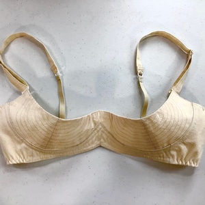 May include: A beige bra with adjustable straps. The bra is made of a soft, breathable fabric and has a simple, classic design.