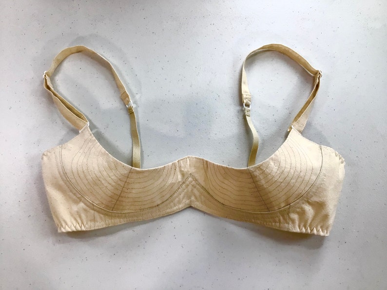 May include: A beige bra with adjustable straps. The bra is made of a soft, breathable fabric and has a simple, classic design.