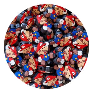 May include: A pile of colourful Mario-themed charms. The charms depict the character in his red hat, blue overalls, and brown shoes. The charms are made of a rubbery material and are black on the back.