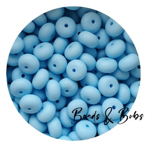 Può includere: Un'immagine ravvicinata di un mucchio di perline di silicone blu chiaro. Le perline sono rotonde con un foro al centro. Le perline sono perfette per realizzare collane, braccialetti e altri gioielli.
