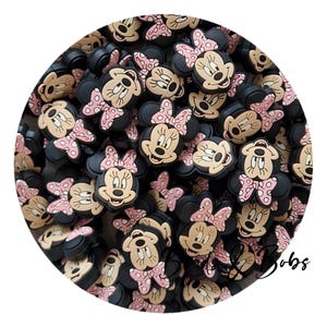 Puede incluir: Un conjunto de abalorios negros con forma de Minnie Mouse, con caras color canela, lazos rosas con lunares y orejas negras. Estos abalorios son ideales para manualidades, la creación de joyas o para añadir un toque de magia Disney.
