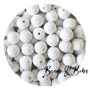 May include: A pile of white, spherical beads with a speckled pattern and grooved texture. The beads are arranged in a circular shape. The text "Beads & Bobs" is written in a cursive font.