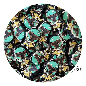 May include: A collection of small, flat, rubberised charms featuring a stylised character in a teal, black, and yellow helmet and armour. The character has a T-shaped visor and a yellow cape. The text "Beads & Bobs" is visible in the lower right.