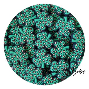 以下が含まれることがあります： ベージュと黒のヒョウ柄模様の緑色のクローバー型チャームのコレクション。チャームは円形に配置されており、聖パトリックの日のクラフトやアクセサリーに最適です。