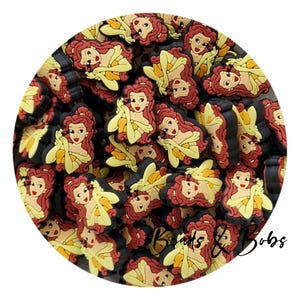 May include: A pile of cartoon character charms. The charms depict a woman with red hair and a yellow dress. The charms have black sides and are arranged in a circle. The text "Beads & Bobs" is visible in the bottom right corner.