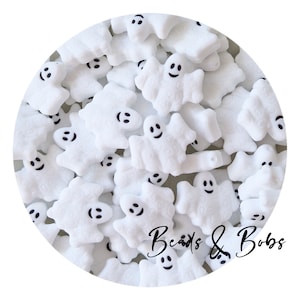 May include: A collection of white ghost-shaped beads with black smiling faces. The beads are scattered, creating a playful and festive arrangement. The text "Beads & Bobs" is written in a cursive font.
