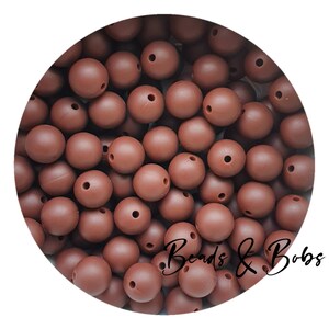 Può includere: Un'immagine ravvicinata di una grande quantità di perline di silicone marroni. Le perline sono rotonde e hanno un foro al centro. Le perline sono perfette per realizzare gioielli, giocattoli per bambini e altri lavoretti.