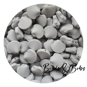 Può includere: Primo piano di un mucchio di perline di silicone grigie a forma di conchiglia. Le perline hanno una superficie testurizzata e un foro al centro. Le perline sono disposte in cerchio, con il testo "Beads & Bobs" visibile nell'angolo in basso a destra.