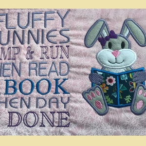 May include: Embroidered design on a pink fabric featuring a gray bunny holding a book with the text "The Fluffy Bunnies Jump & Run Then Read A Book When Day Is Done".