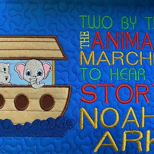 May include: A blue quilted fabric with a brown ark with a hippopotamus and an elephant on it. The text "Two by two the animals marched to hear the story of Noah's Ark" is embroidered in green, red, and yellow thread.