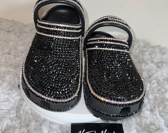 Puede incluir: Sandalias de zueco negras con un diseño completo de pedrería. Las sandalias tienen una correa negra con pedrería y una suela negra.