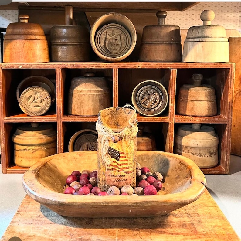 May include: A wooden shelf with a variety of antique wooden cookie cutters and molds. The shelf is filled with different shapes and sizes of cutters, including a heart, a star, and a flower. There is also a wooden bowl with red berries in the foreground.
