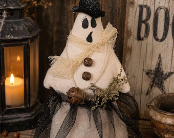 May include: A fabric ghost figurine wearing a black glittery hat, a frayed beige scarf, and a black tulle skirt. The ghost features painted black eyes and mouth, two rusty metal jingle bells on the chest, a larger bell, and a small metal key.
