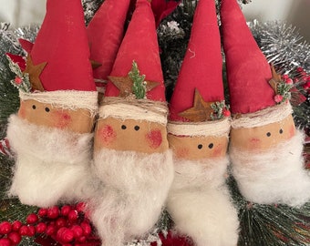 Op de afbeelding: Een set van vier stoffen kerstman-ornamenten met hoge rode puntmutsen, elk bekroond met een klein metalen belletje. De figuren hebben beige gezichten met geschilderde zwarte ogen, roze wangen en lange witte baarden van imitatiebont.