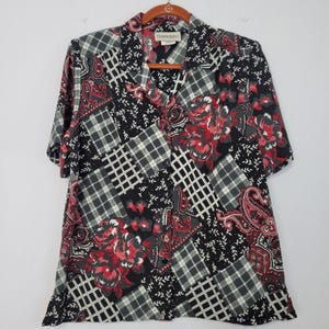 May include: A short-sleeved button-down shirt featuring a patchwork design of black, white, and red patterns including floral motifs, paisley swirls, and plaid grids. The shirt has a collar, a front button closure, and a label reading DONNKENNY.