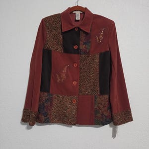 May include: A long-sleeved button-down jacket in shades of terracotta, featuring a patchwork design of solid fabric, textured brown tweed, and floral print panels. The jacket includes embroidered leaf details and a classic collar.
