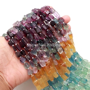 Könnte beinhalten: Stränge bunter Fluorite-Edelsteinperlen in Lila, Grün, Gelb und Orange. Die rechteckigen Perlen sind aufgereiht. Der Text "JaipurNaturalBeads" ist sichtbar.