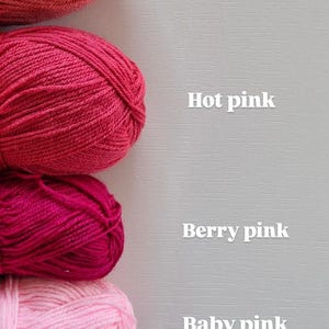 May include: Five skeins of yarn arranged vertically, labelled with white text: Coral, Hot pink, Berry pink, Baby pink, and Soft pink. Each skein features a distinct shade of pink or coral, showcasing a smooth, twisted fibre texture in a stack.