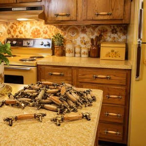 May include: A large collection of cabinet pulls featuring a central wooden handle with a light brown grain, flanked by antique brass-toned metal ends. Each pull has two mounting points, showcasing a classic design for kitchen cabinetry hardware.