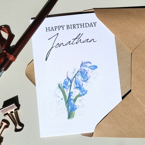 May include: A white card with a bluebell flower illustration and the text "Happy Birthday Jonathan". The card is in a brown envelope.