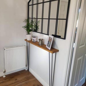 K&ouml;nnte beinhalten: Ein Konsolentisch aus Holz mit schwarzen Haarnadelbeinen. Der Tisch ist mit einer Topfpflanze, Kerzen und einem gerahmten Foto dekoriert. Der Tisch steht an einer wei&szlig;en Wand mit einem schwarzen Spiegel dar&uuml;ber.