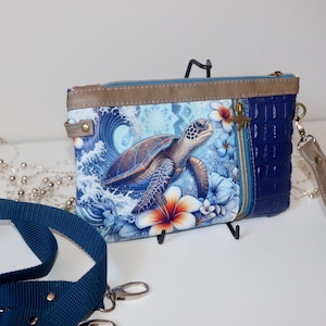 May include: A blue and brown clutch bag with a sea turtle design and a zip fastening. The bag has a detachable strap.