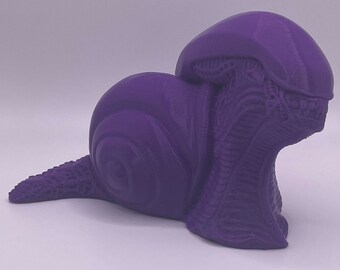 May include: A purple 3D printed figurine of an alien creature in a curled up position, resembling a snail.
