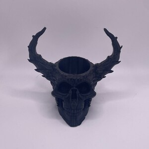 May include: Black skull planter with horns, made of 3D printed plastic. The planter has a round opening at the top for planting.