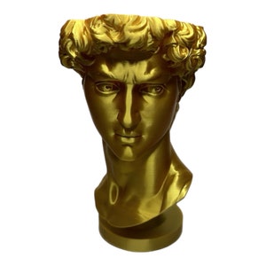 May include: A gold-colored bust sculpture of a man with a detailed face and curly hair. The sculpture is on a round base.