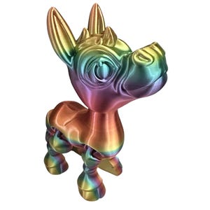 May include: A 3D-printed figurine of a stylized creature, featuring a rainbow gradient of colors. The figure has large eyes, pointed ears, and a small horn. The creature is posed in a standing position, with its head tilted upwards.