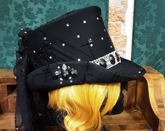 Può includere: Un cappello a cilindro nero con un velo in rete nera e strass. Il cappello è su una testa di manichino nera con capelli biondi.
